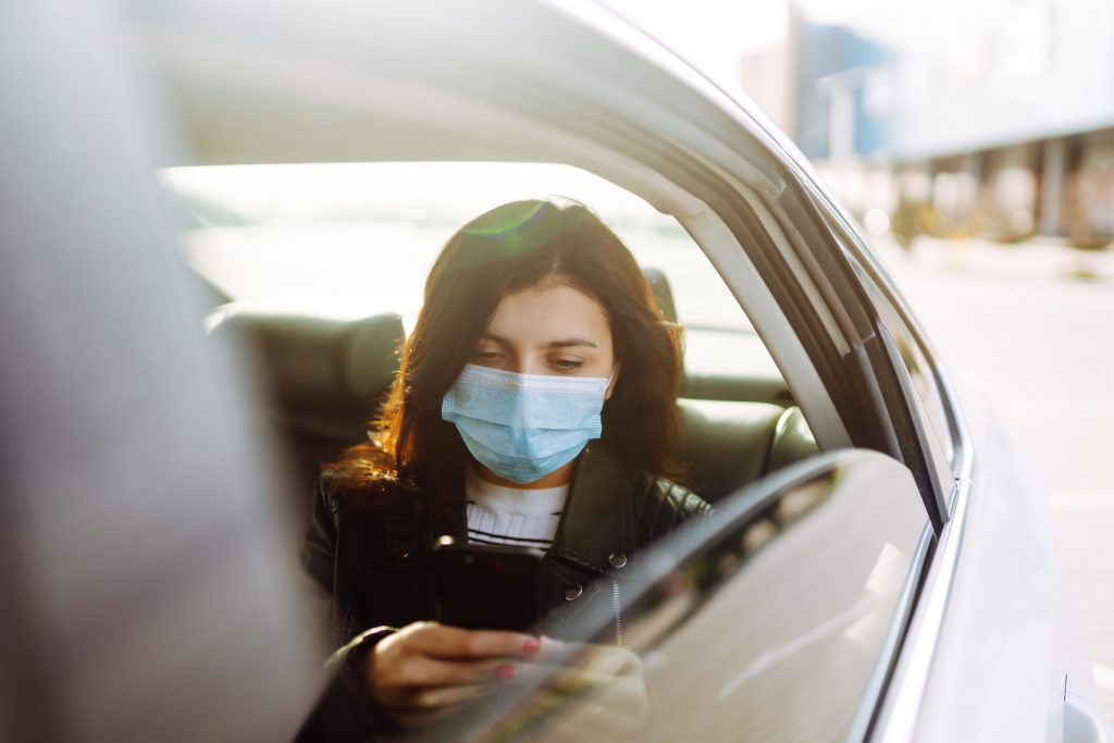 Girl in protective sterile medical mask on her face is talking on his phone in taxi. Covid-19